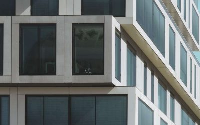 A vertical shot of a grey concrete building with big windows under the blue sky