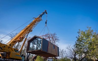 A powerful truck crane is employed in the process of moving a modular home from a truck trailer to a land plot.