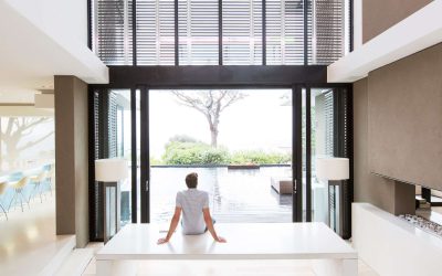 Rear view of man sitting on table looking at swimming pool through open patio door